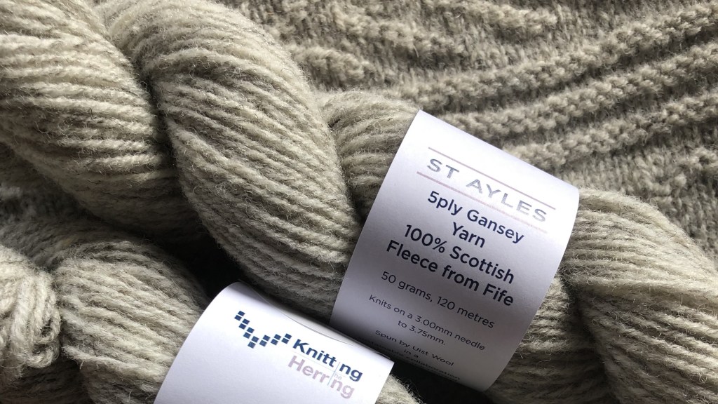 Two hanks of grey wool with labels reading: ST AYLES 5ply gansey yarn, 100% Scottish fleece from Fife, 50 grams, 200 metres, Knits on a 3.00mm needle to 3.75mm, spun by Uist Wool. Knitting the Herring