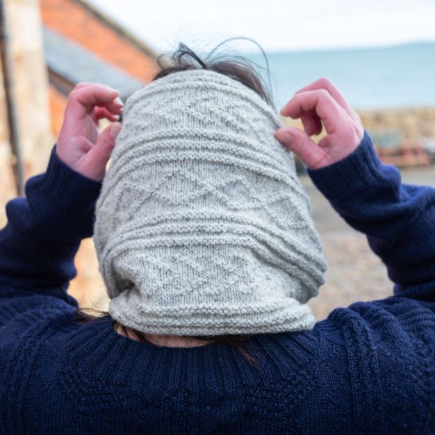 Head and shoulders of a woman wearing a grey knitted Caiplie cowl.