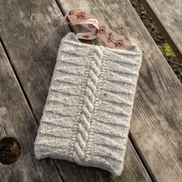 A book inside a grey knitted Cutty Skelly book cover, lying on a wooden table.